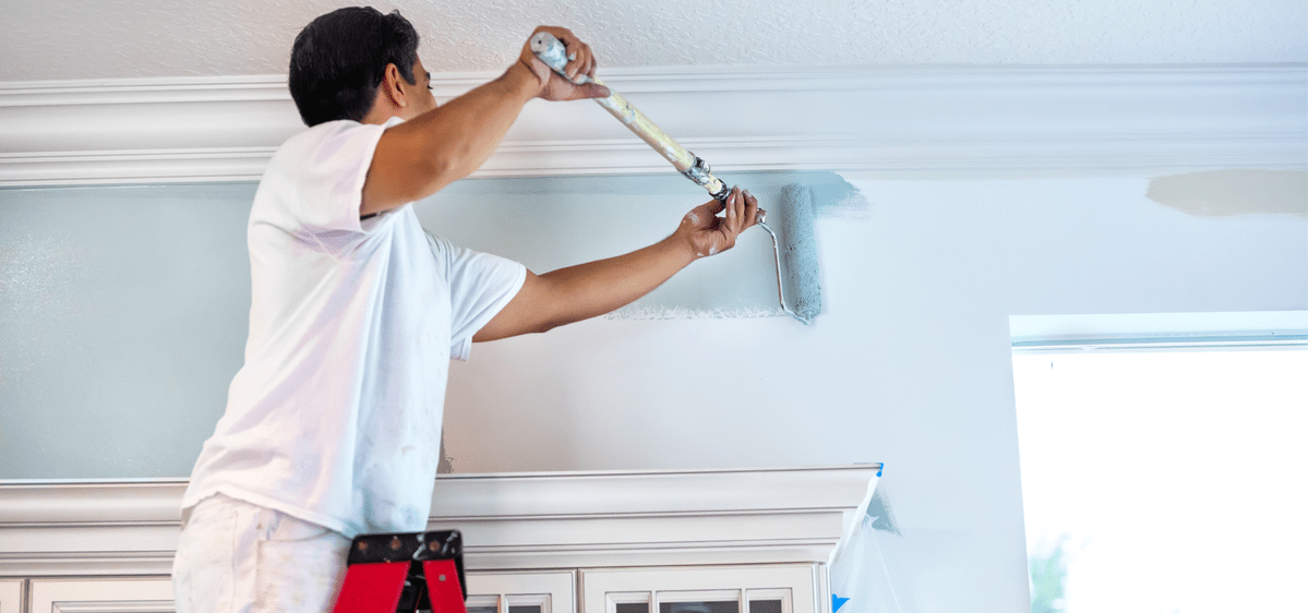 Man Painting Wall With Roller Spring Refresh Blog Feature Image. Man painting a wall in a light blue color