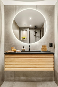 Modern bathroom with a round mirror, wooden vanity, and black countertop