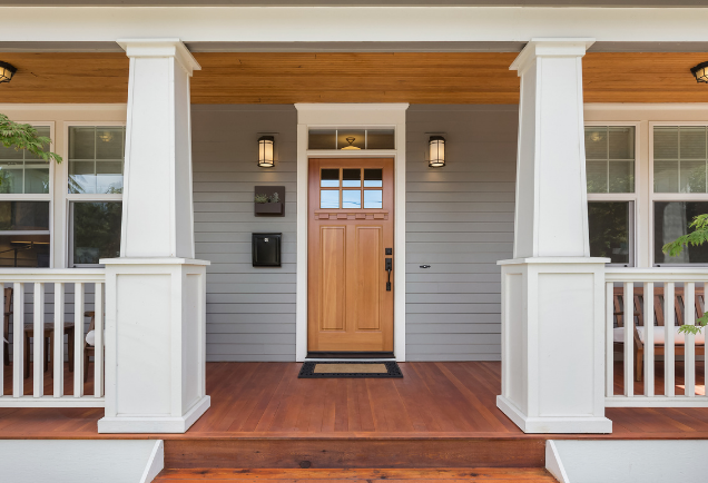 Front porch of a modern home with a wooden door and white columns.