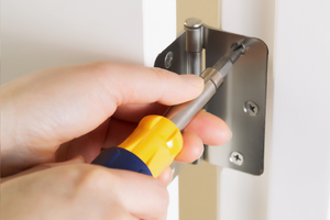 Person using a screwdriver to tighten a door hinge screw.