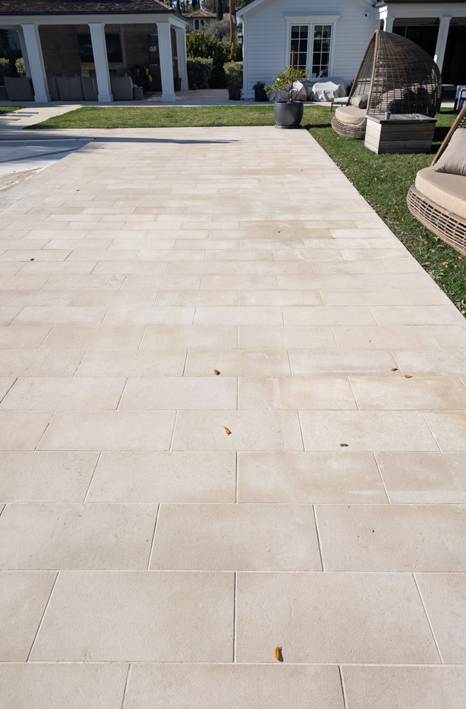 Beige stone patio with outdoor furniture and green lawn